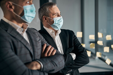 Two businessmen in medical masks standing in office