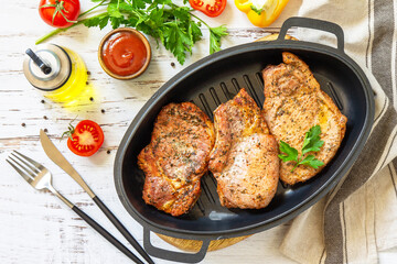 Barbecues parties menu. Baked meat pork loin on the bone with spices in a cast iron pan on rustic wooden table. Top view flat lay.