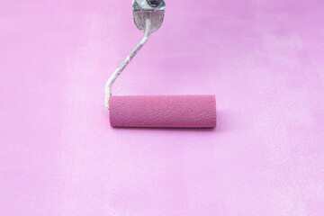 Woman painting a piece of furniture with a paint roller in malva color