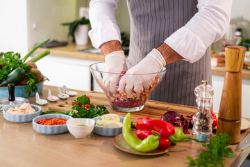 The cook mixing the spices and the meat for burger with onion and bacon in a bowl