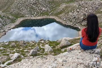 Girl stting on the stone and looking to the Small Arashan lake. Small Arashan lake is about at an altitude of 2880 meters above sea level. Namangan region, Uzbekistan