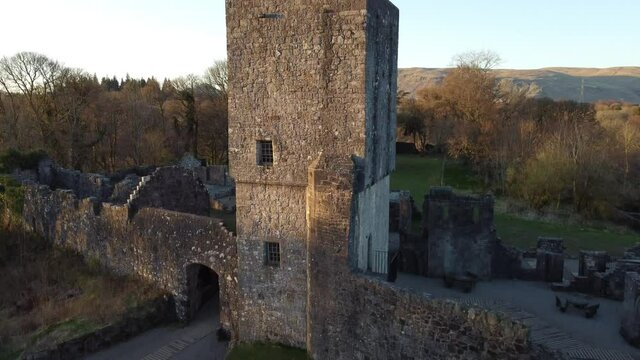 Ascending aerial footage over a castle ruin with square stone tower and scenic view to hills in the distance.