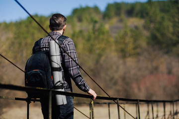A man with a backpack walks across the suspension bridge on the mountains. 