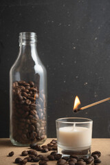 Lighting a candle with a match, a bottle with coffee beans in the background