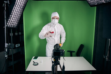 Male doctor in protective mask and suit recording video for blog