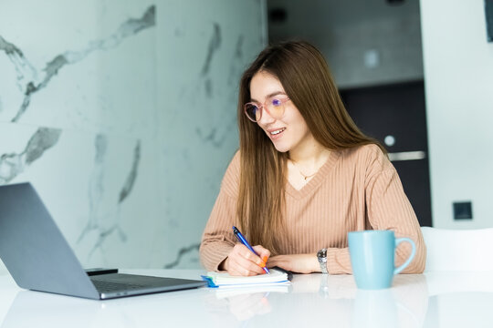 Woman working on laptop at home on kitchen. writing on notepad. Woman trying to find a job. Crysis. Girl styding from home