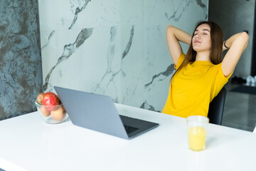 Young pretty woman relaxing after using laptop while sitting at kitchen