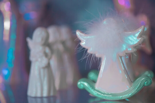Small white marble figurine of an angel with fluffy wings on a colorful light blue pink blurred bokeh background. Back view. Close-up