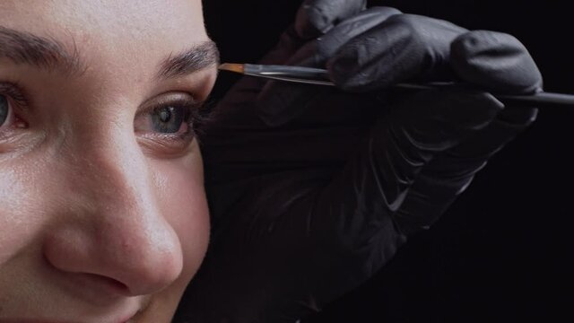 Eyebrow make-up. Professional make-up artist paints eyebrows of young woman with brush. Close up.