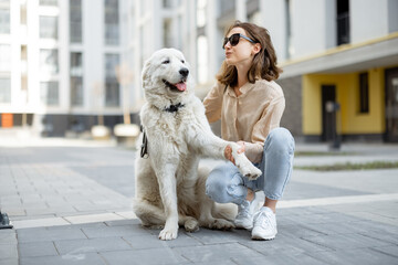 Cheerful woman play and hugs with her big white happy dog on the street. Pet friendly and pet care concept. Animal lover. Dog gives a paw