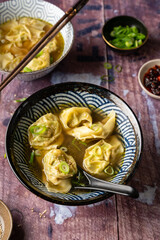 Side view of two bowls of home made vegan wonton soup served on wooden table with chopsticks with chili crisp oil