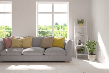 Fototapeta premium White living room with sofa and summer landscape in window. Scandinavian interior design. 3D illustration
