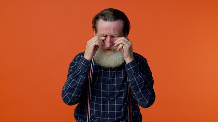 Disappointed upset elderly old bearded gray-haired man wipes tears and cries from despair, being...