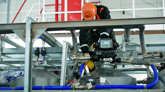 A worker wearing a helmet and gloves, removes the pipes to the distribution unit to control the filtration of water in the tank. Industrial profession. Dangerous job
