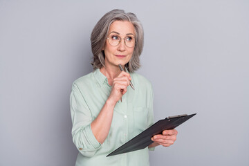 Portrait of attractive minded gray-haired woman creating writing to-do list isolated over grey...