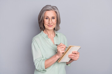 Photo of happy lovely pretty smiling mature woman author in glasses writing in notebook isolated on...