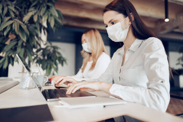 Two female colleagues working in office together wearing medical masks