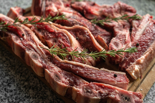 Close up of short rib strips seasoned with rosemary on a wooden board.
