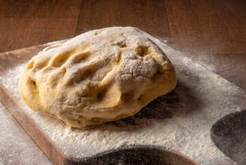 Dough being sprinkled with wheat on wood, selective focus.