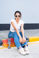 Asian cute girl or woman sit on street, place her legs on skateboard, and looking straight ​in...