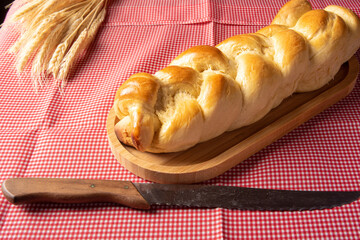 Homemade bread, braided bread on wood and a red and white checkered tablecloth, a knife and a branch of wheat, selective focus.