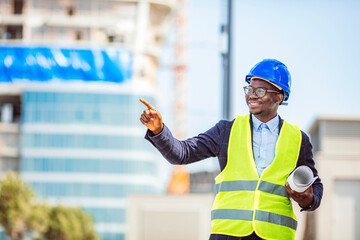Portrait of smiling engineer in hardhat standing at construction site holding blueprint. Portrait...