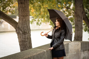 Brunette girl in a black jacket stands on the river embankment