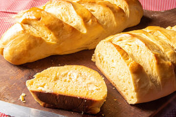 Homemade bread, sliced ​​homemade bread with butter on wood and a red and white checkered tablecloth, a knife and a bunch of wheat, selective focus.