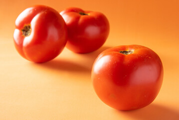 Tomatoes, three tomatoes arranged on an orange surface, selective focus.