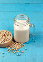 Soy milk in transparent glass with soybeans in wooden bowl on blue wooden table. Healthy concept.