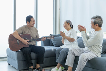 Old men and women singing to music with guitar in the living room. Senior friends group hangout,...