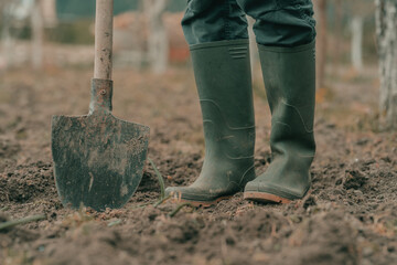 Farmer in rubber boots using spade gardening equipment in garden