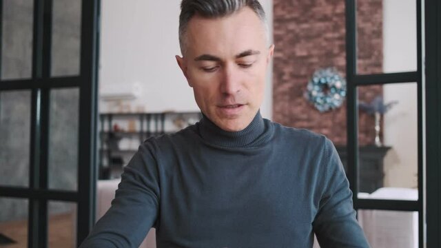 A smiling man sitting at the table and talking affably on the video call in the room