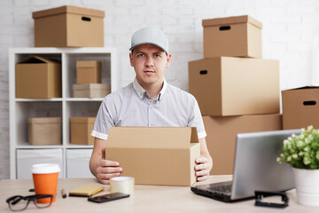 Young man with laptop preparing parcels for shipment to client in post office.