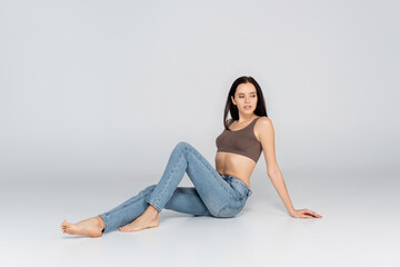 Fototapeta na wymiar brunette woman with perfect body sitting on grey in jeans and bra