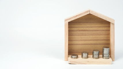 Property investment and house mortgage financial concept, Stacking coins with wooden house backdrop on white background.
