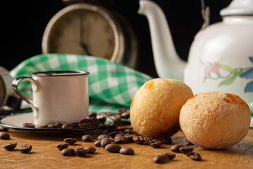 coffee table in Brazil in detail with antique clock, cups, coffee beans and cheese bread on rustic wood, with green and white checkered tablecloth, selective focus.