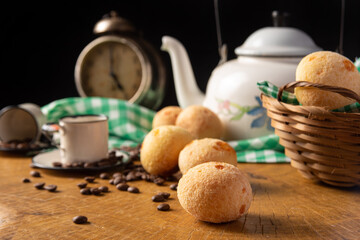 coffee table in Brazil in detail with antique clock, cups, coffee beans and cheese bread on rustic wood, with green and white checkered tablecloth, selective focus.