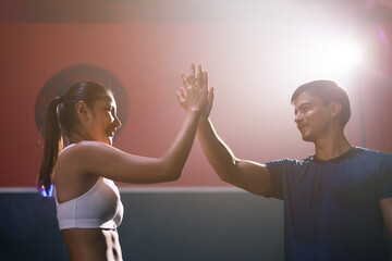Young happy fit Asian woman in sportswear and young fit Caucasian man buddy making hi five with hands, greeting befor exercise at the gym.
