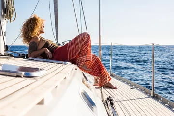 Fotobehang Attractive woman sailing on a yacht on summer day - relax and vacation lifestyle female people laying on the deck of the sailboat enjoying the sun and freedom - blue ocean background © simona