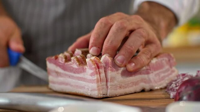 The cook is cutting bacon on a wooden board in kitchen