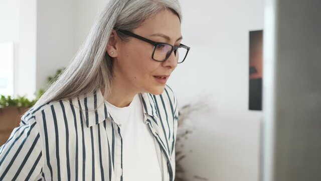 A side view of a pretty nice elder woman wearing glasses is using a vending machine in the apartments
