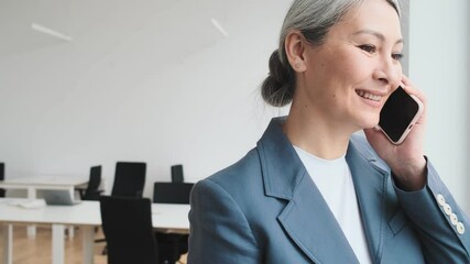 A beautiful elder businesswoman is talking on her smartphone in the office