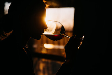 Silhouette of a young woman drinking red wine in sunset light.