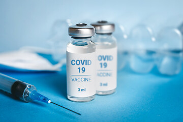 Coronavirus vaccine. Ampoules with coronavirus vaccine and a syringe on blue background. Covid-19 treatment