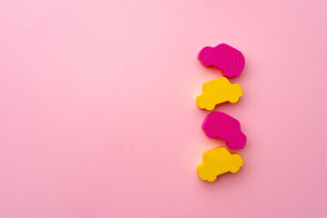 Wooden figures of toy cars on pink paper background