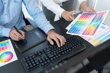 graphic designer team working on web design using color swatches editing artwork using tablet and a stylus at desks In creative office