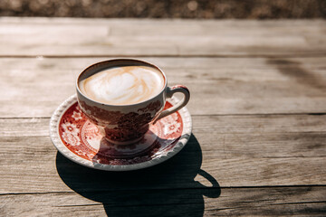 Vintage cup of cappuccino on a wooden table at a terrace, outdoors, in sun light.