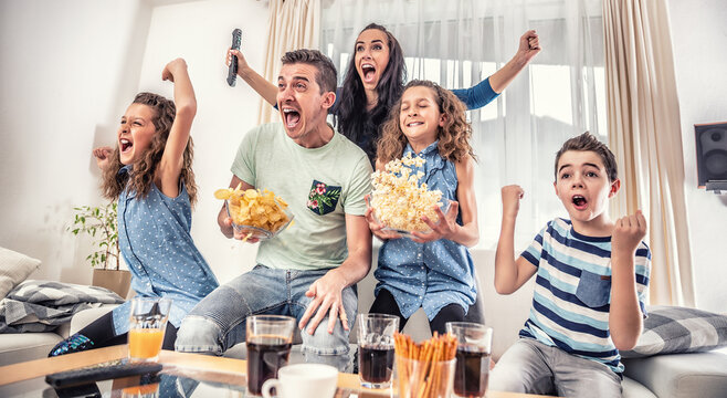 Family Watching Sports Match On Tv At Home, Cheering And Shouting Goal With Hands Up, Spilling Chips And Popcorn From Excitement