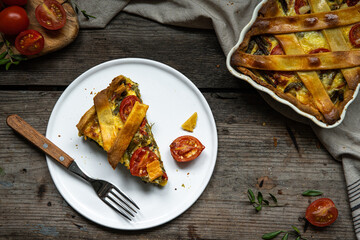 Piece of freshly baked savory pie (quiche) with green beans, peas, bell pepper, cherry tomatoes and cheese  on white plate on rustic wooden table.